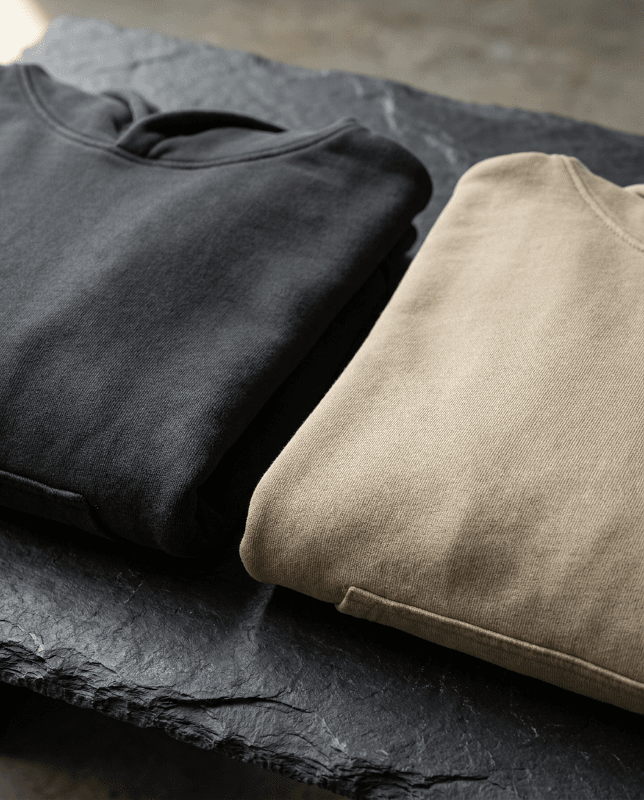 The Founding Hoodie in charcoal and sand, folded on slate.